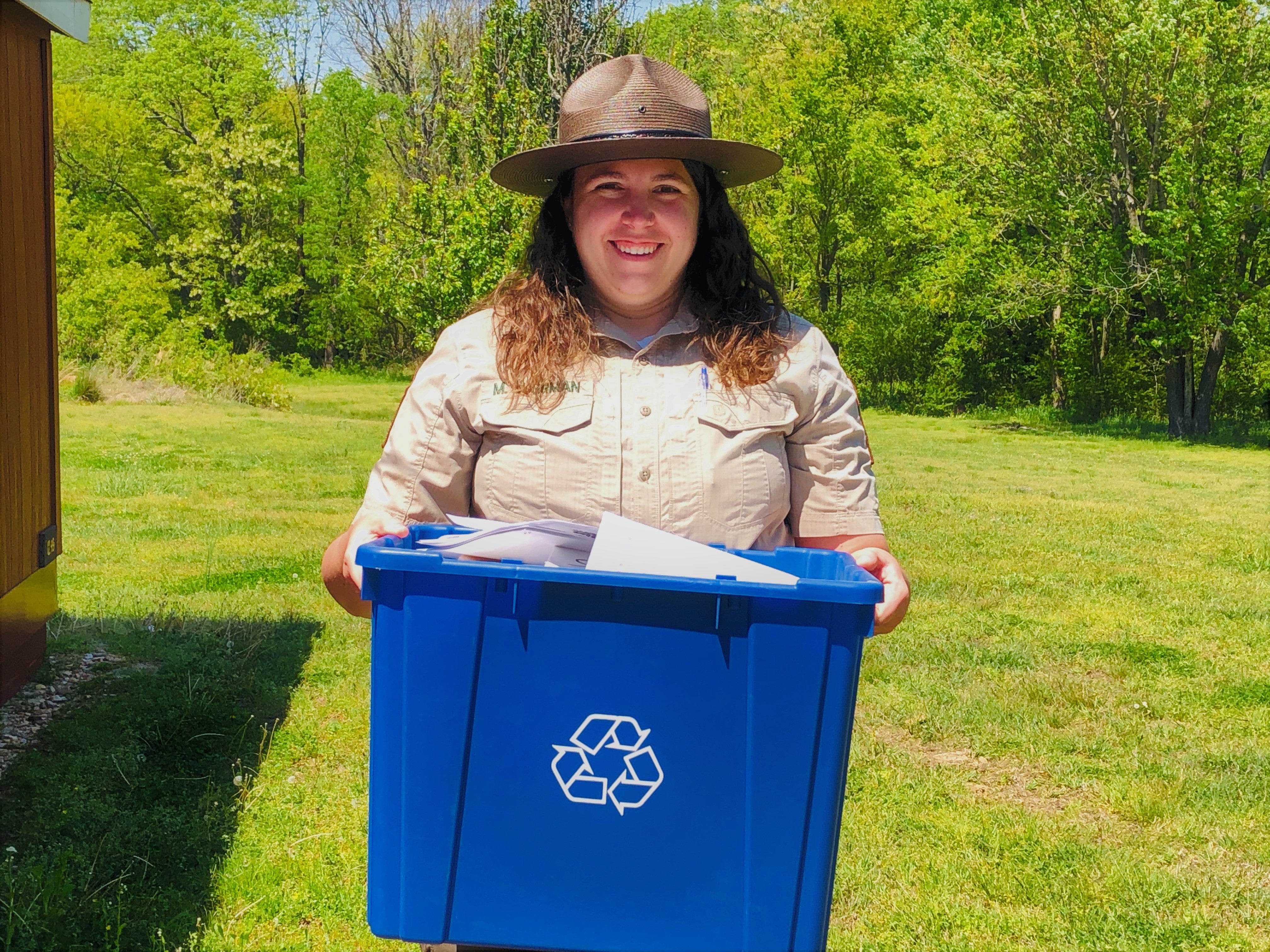 Adult female smiling and holding a blue recycling box filled with paper 